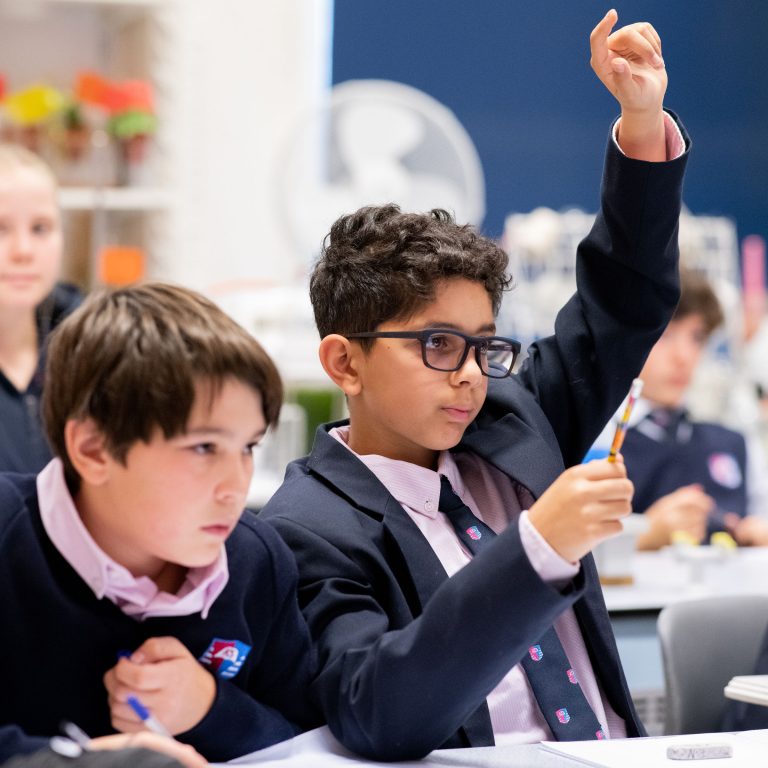 A student putting their hand up as other students in the background look on