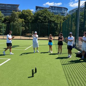 A student raising a trophy as the other students clap on the tennis court