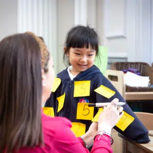 A young pupil and teacher writing on notes for an activity at the Knightsbridge School private preschool